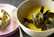 Bowl of saffron mussel stew with a yellow broth, a plate with shells to the left
