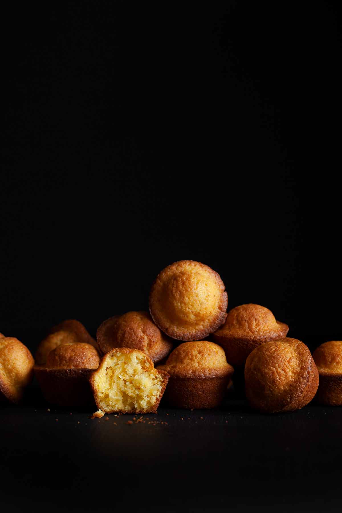 Portuguese mini lemon-orange cakes scattered on a black background with one torn in half.