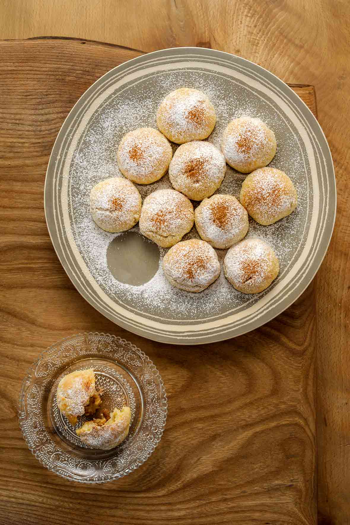 A plate of round Greek biscuit cookies with an apple filling, all dusted with powdered sugar