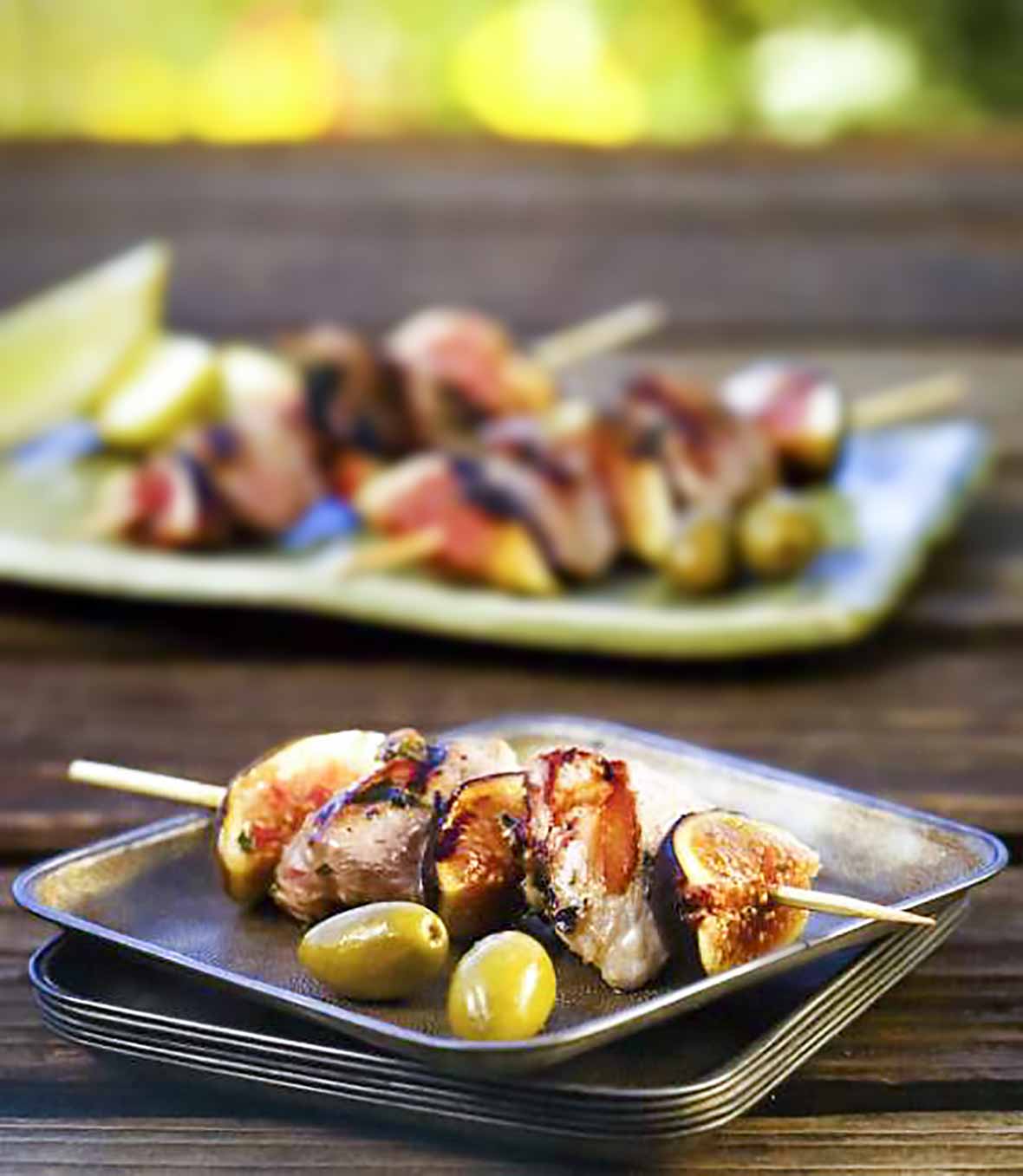 Duck, olive, and fig Skewers on a square plate.