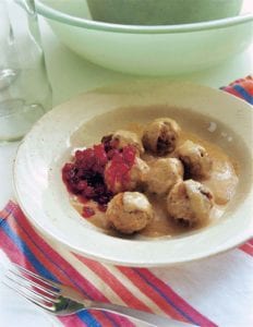 A white bowl filled with seven Finnish meatballs, sauce, and topped with lingonberry jam.