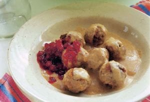 A white bowl filled with seven Finnish meatballs, sauce, and topped with lingonberry jam.
