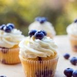 Several blueberry cupcakes topped with whipped cream and fresh blueberries.