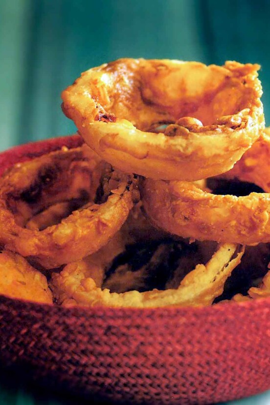 A red woven basket with a pile of buttermilk onion rings