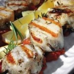 Grilled scallops are threaded on rosemary skewers and sitting on a bed of tomato chutney
