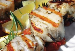 Grilled scallops are threaded on rosemary skewers and sitting on a bed of tomato chutney