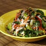 Poached chicken and cabbage salad piled in a yellow dish, garnished with fried shallots