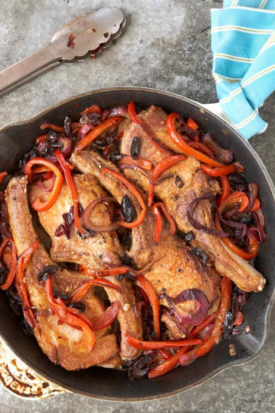Brined pork chops cooked with red peppers, onions, black olives, and garlic in a skillet on stone