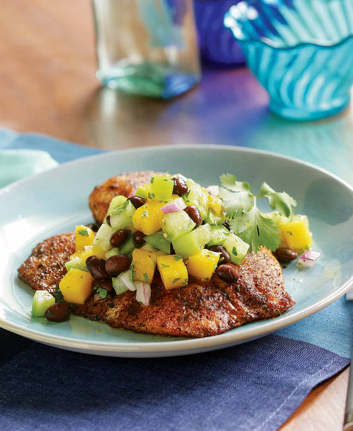 Spice-rubbed tilapia with mango salad on a pale blue plate with blue glass in the background