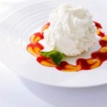 Plate of three milks cake, topped with whipped cream, with red and orange sauces