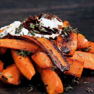 Burnt carrots, goat cheese, and garlic crisps piled on a wooden surface, garnished with thyme