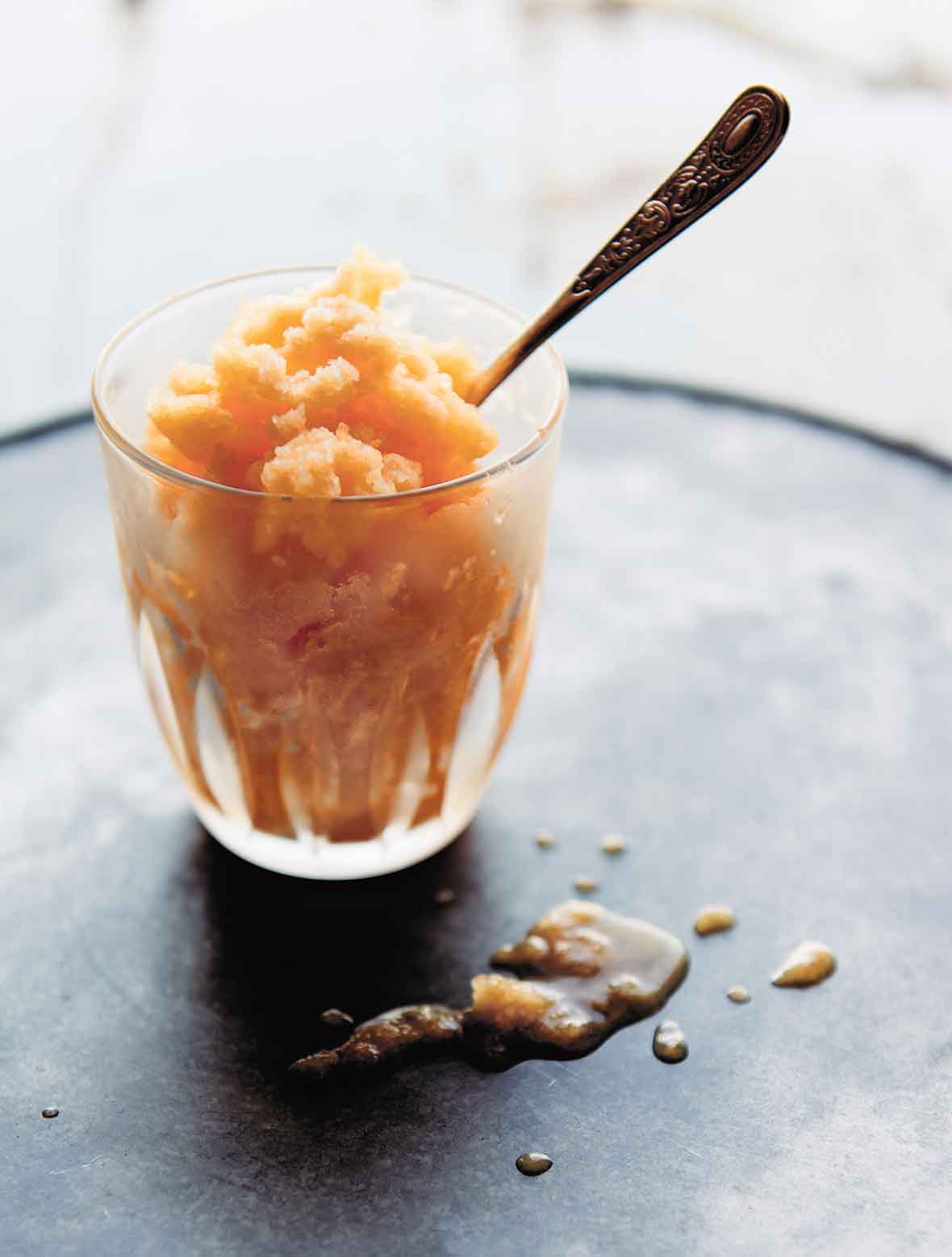 A small glass filled with cantaloupe granita and a spoon sticking out of it.