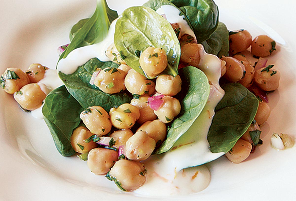 A serving of chickpea and spinach salad with cumin, red onion, and yogurt dressing on a white plate.
