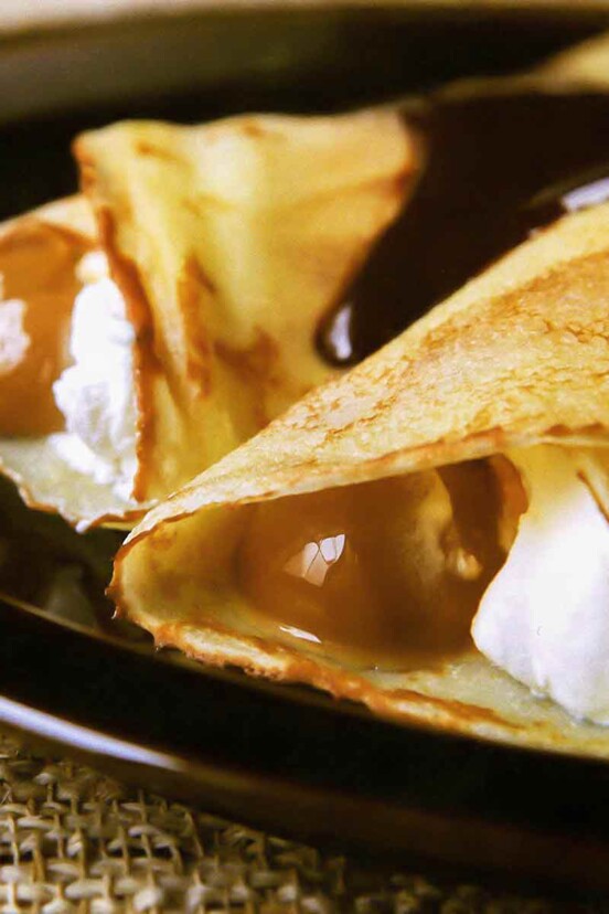 A plate with two dulce de leche crepes filled with whipped cream and topped with chocolate sauce.