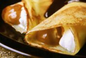 A plate with two dulce de leche crepes filled with whipped cream and topped with chocolate sauce.