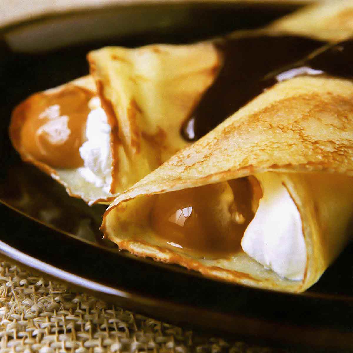 A plate with two dulce de leche crepes filled with whipped cream and topped with chocolate sauce.