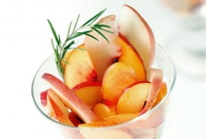 Slices of peaches and nectarines with rosemary and honey syrup and a sprig of rosemary in a glass.
