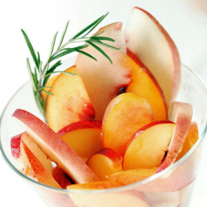 Slices of peaches and nectarines with rosemary and honey syrup and a sprig of rosemary in a glass.