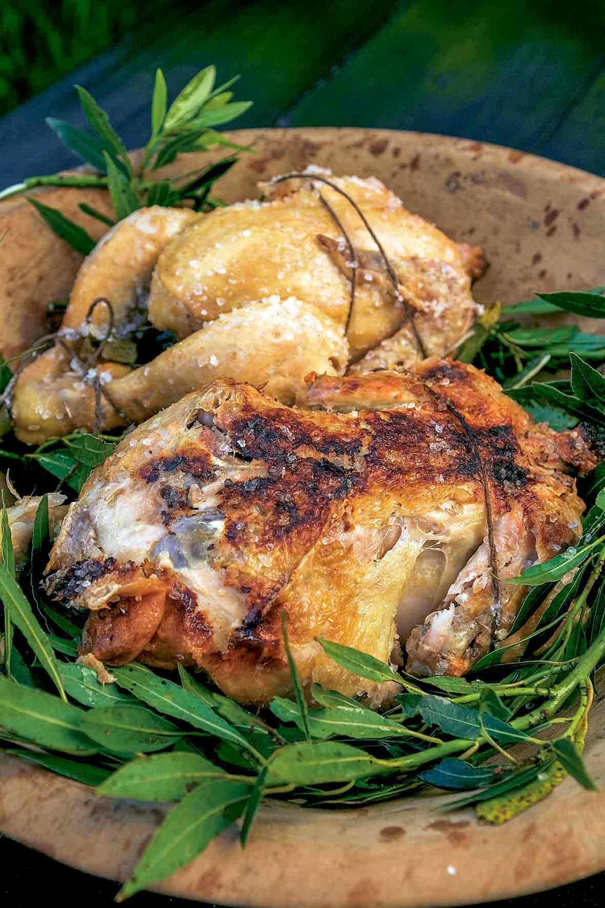 Two salt crust chickens on a bed of leaves and wooden plate