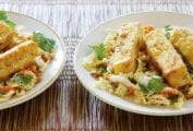 Two plates of warm cabbage salad with fried crispy tofu, carrots, cilantro on woven placemats