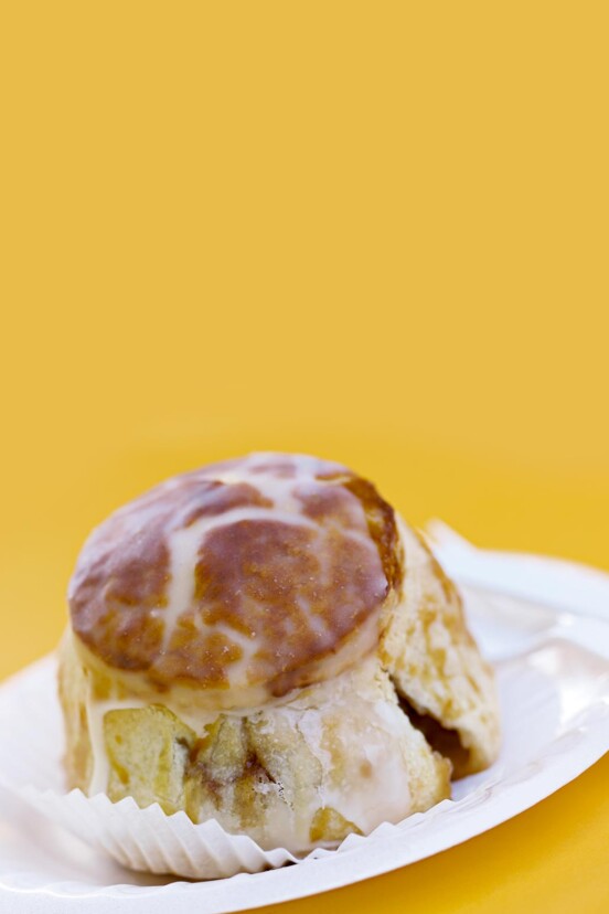 A large glazed apple dumpling on a white plate against a yellow background