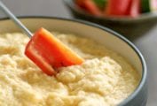 A carrot dipped into A bowl of cauliflower Asiago cheese fondue