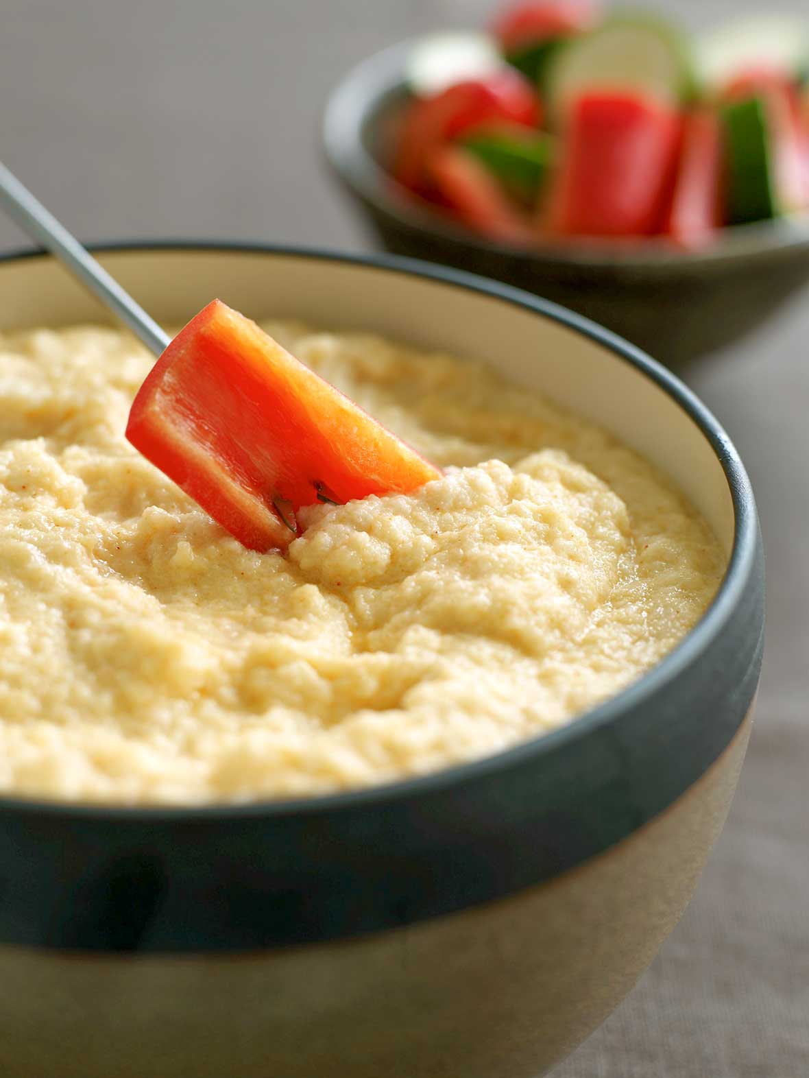 A red pepper dipped into A bowl of cauliflower Asiago cheese fondue