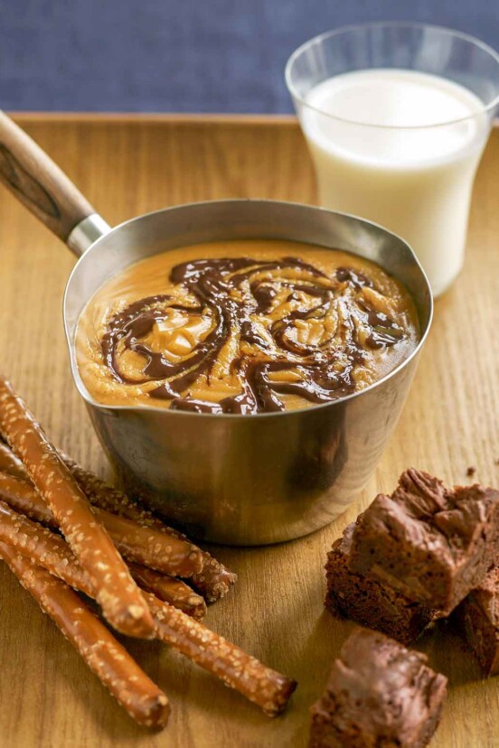Pot of peanut butter chocolate fondue; pretzels and brownies, a glass of milk