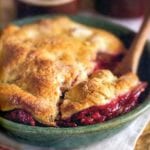 A pear and raspberry pandowdy or cobbler in a green bowl with a pastry top, wooden spoon inside.