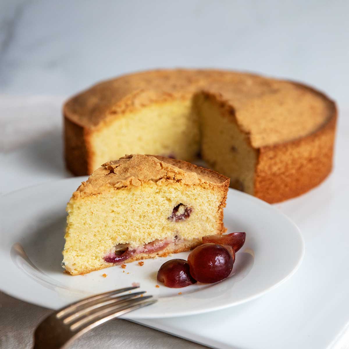 A close-up image of a Semolina-Olive Oil Cake with Drunken Grapes, garnished and ready for serving.
