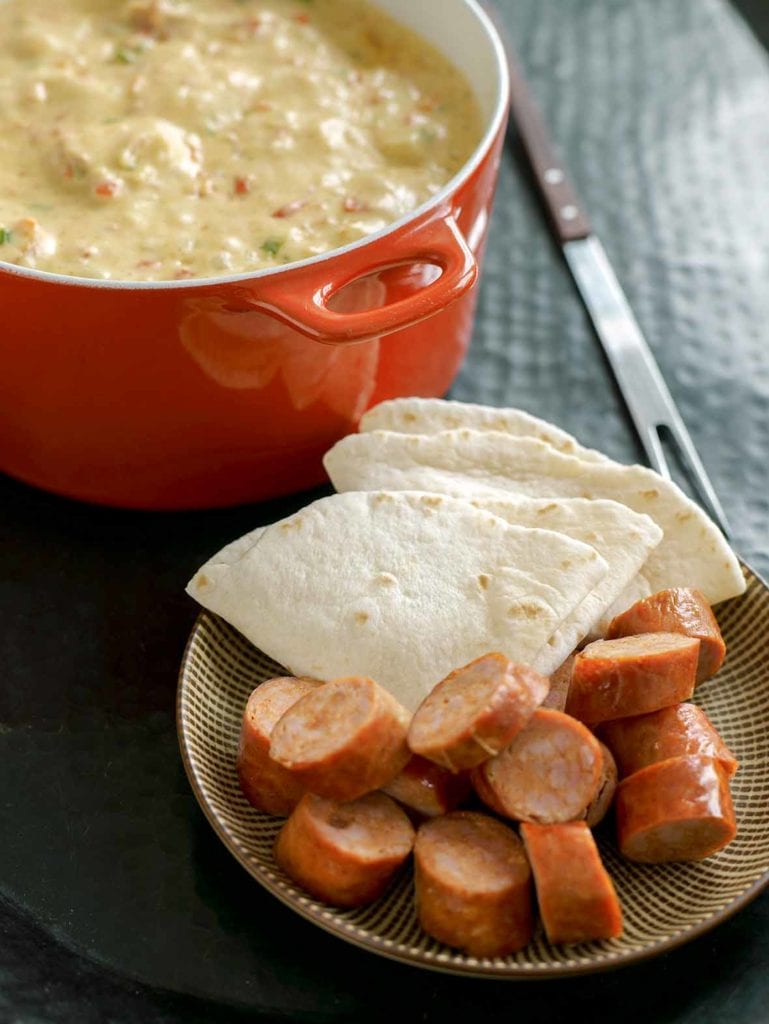 Pot of chile cheese fondue, a plate of chorizo, and tortillas