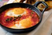 Two eggs in a tomato sauce, topped with a sprig of thyme in a cast iron skillet