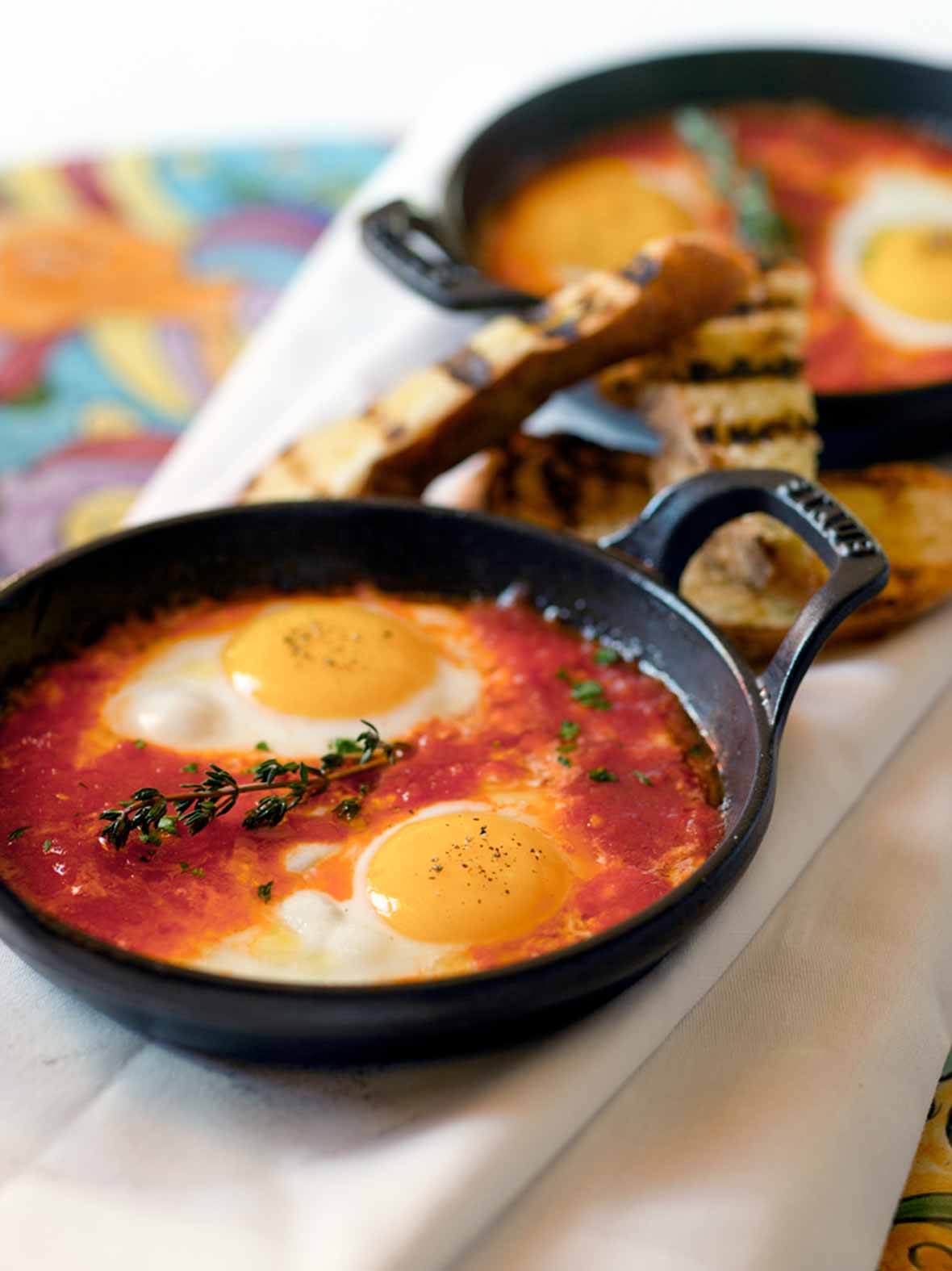 Two eggs in a tomato sauce, topped with a sprig of thyme in a cast iron skillet.