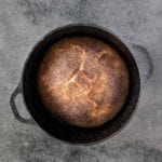Cast-iron pot with a loaf of Jim Lahey's no-knead whole-wheat bread on a gray background.