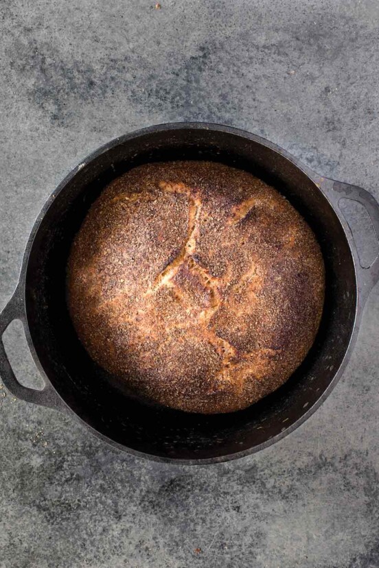 Cast-iron pot with a loaf of Jim Lahey's no-knead whole-wheat bread on a gray background.