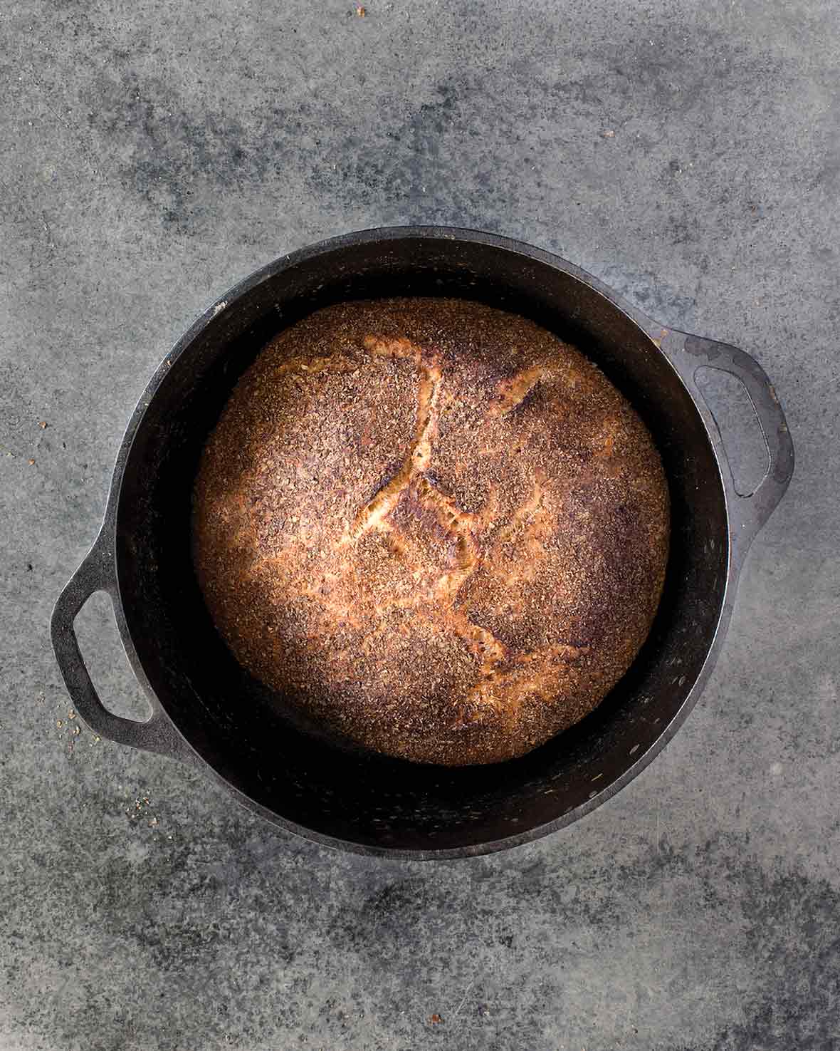 Cast-iron pot with a loaf of Jim Lahey's no-knead whole-wheat bread on a gray background.