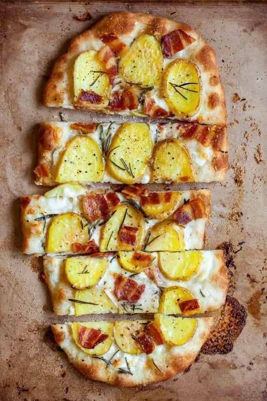 A sliced oval-shaped potato bacon pizza.