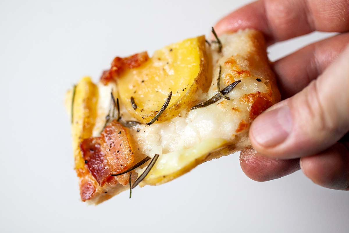 A person holding a slice of potato bacon pizza.