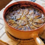Ribollita, or Italian bread soup, in a crock topped with overlapping baked onion slices