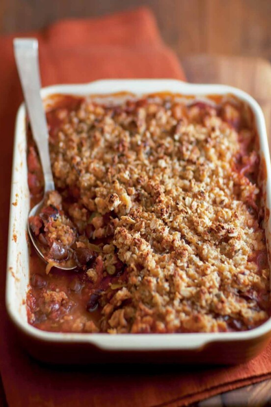 A rectangular casserole dish filled with spicy tomato crumble, and a spoon resting in it.