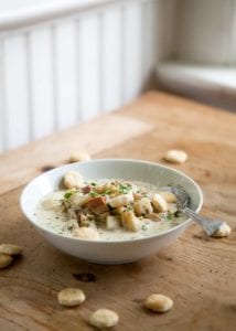 Steamer Clam Chowder in a white soup bowl on a wooden kitchen table surrounded by oyster crackers.