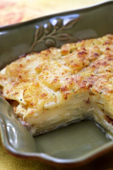 A deep baking dish containing celery root and potato gratin with one piece missing