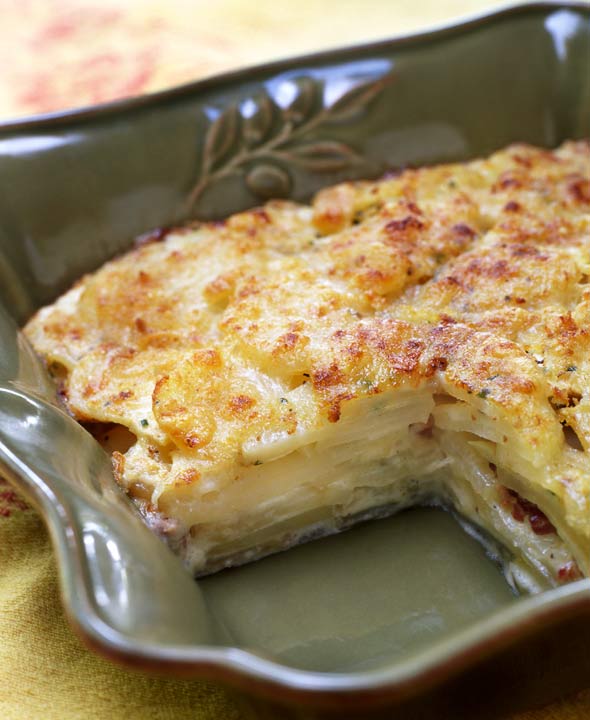 A deep baking dish containing celery root and potato gratin with one piece missing