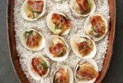 Clams casino, covered with slices of bacon and herbed butter, sit in a large pottery dish filled with rock salt.