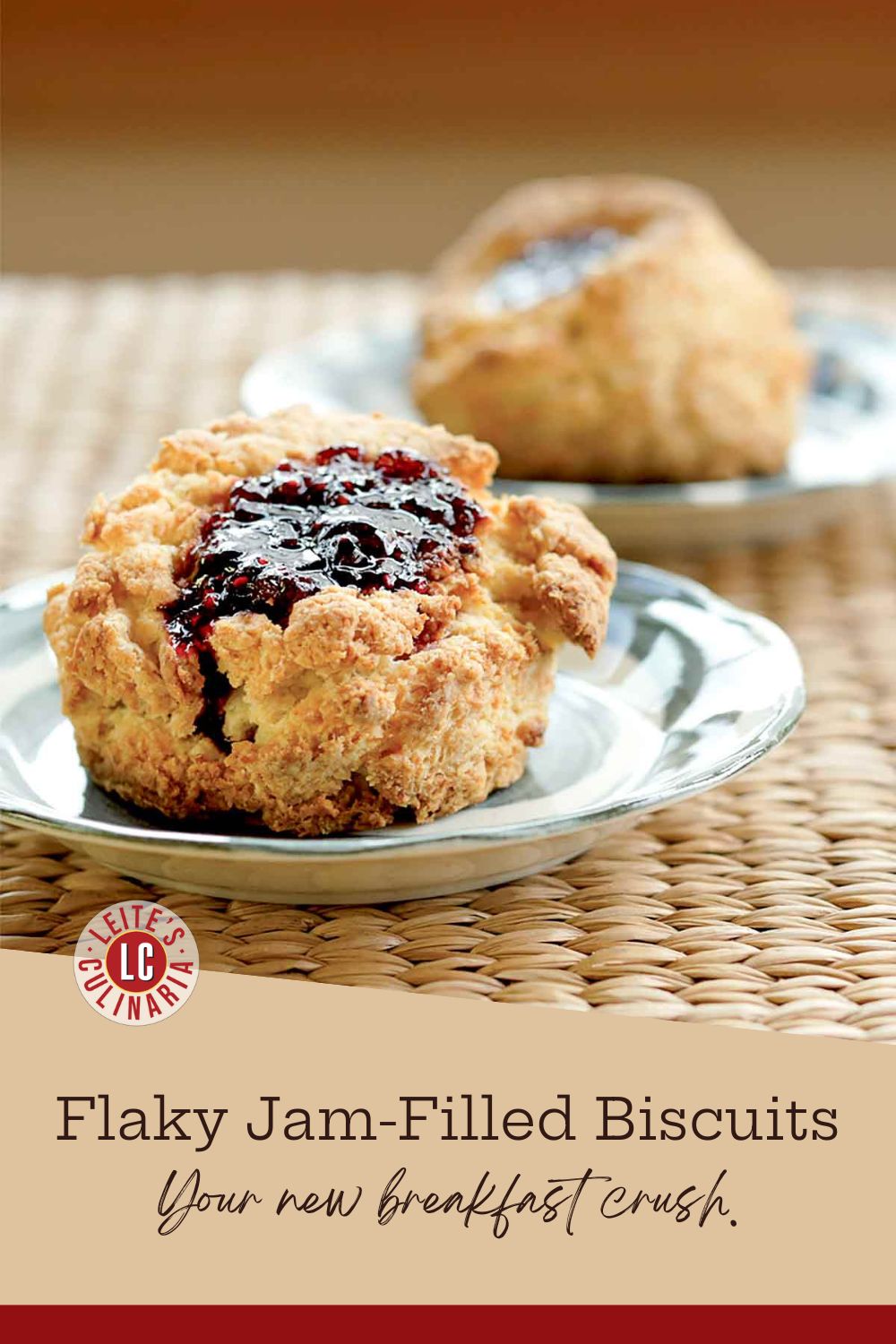 A golden-brown buttermilk biscuit filled with vibrant jam on a white plate, set on a woven mat. The jam drips down the sides.