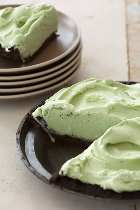 Grasshopper pie in a metal pie pan with a cut out slice sitting on a stack of plates in the background.