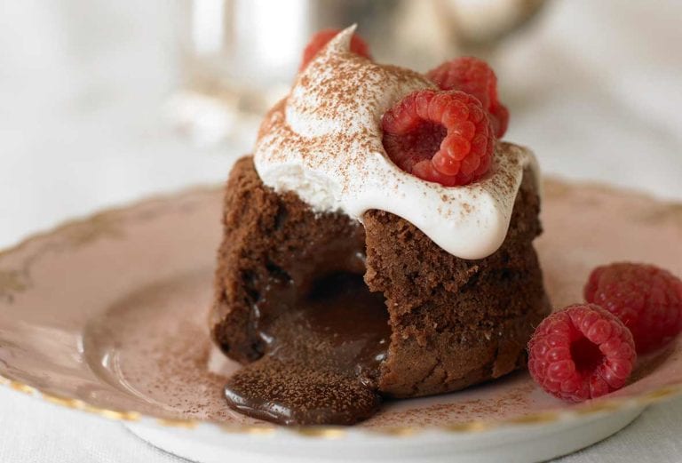 Molten chocolate cake, a wedge cut from it, with chocolate oozing; whipped cream on top, on a plate