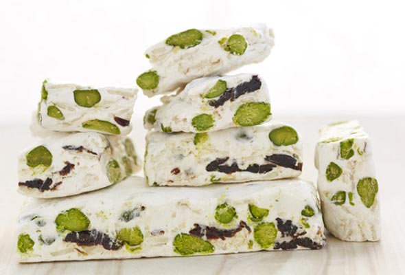 Nut and cherry nougat cut into squares and piled up against a white background.