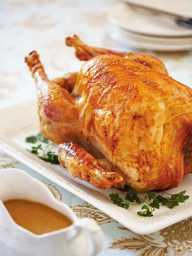 An old-fashioned roast turkey on a white platter, with gravy in a boat beside it.