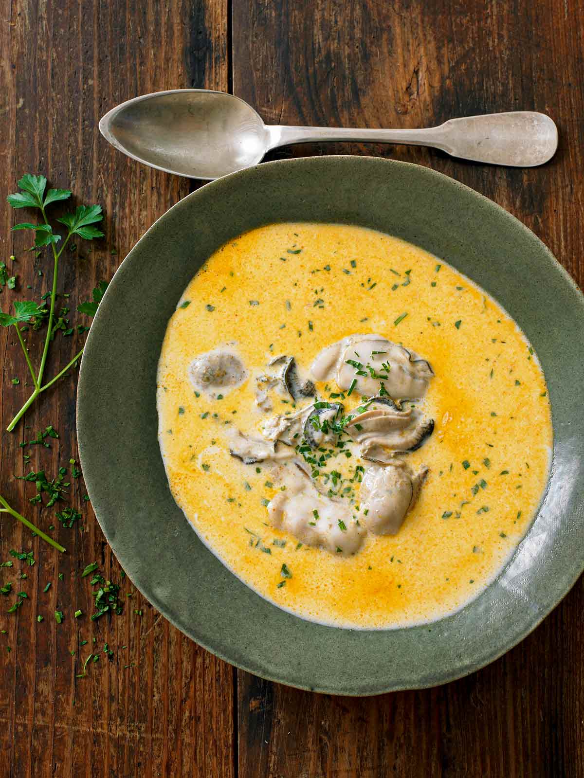 A ceramic bowl filled with oyster stew with several oysters in the center and a spoon resting beside the bowl.